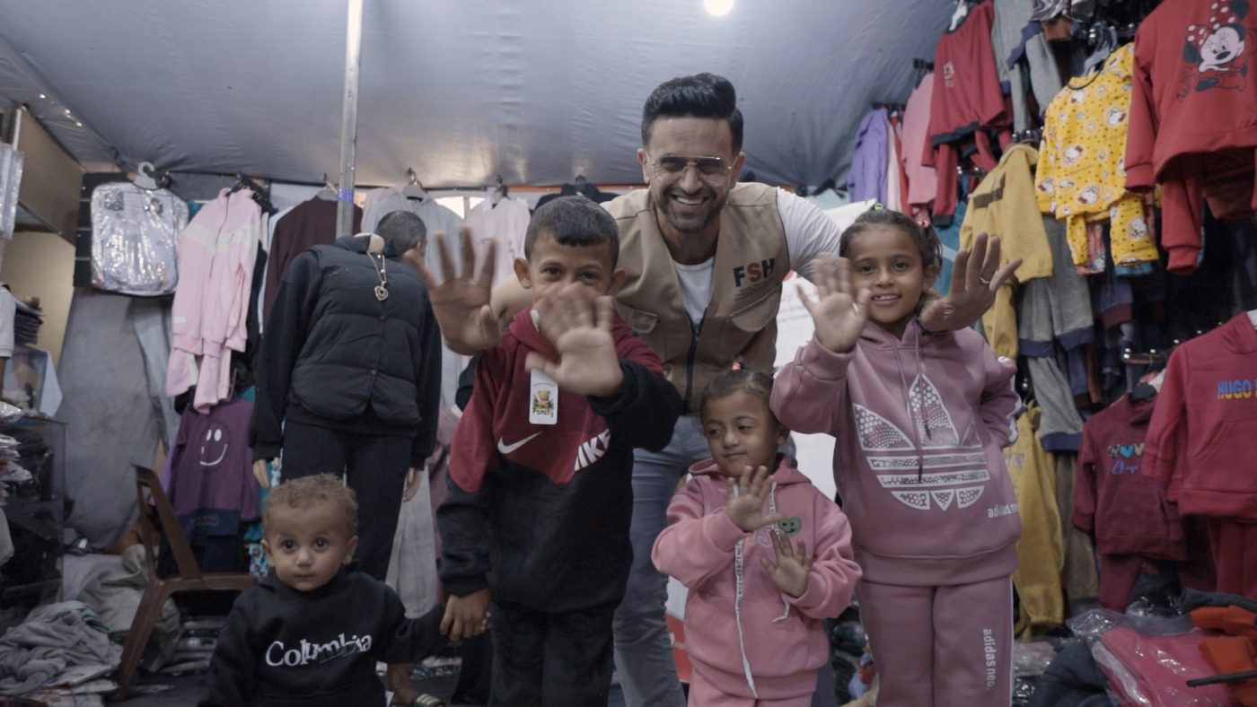 Children in Gaza waving in their new winter clothes with an FSH team member