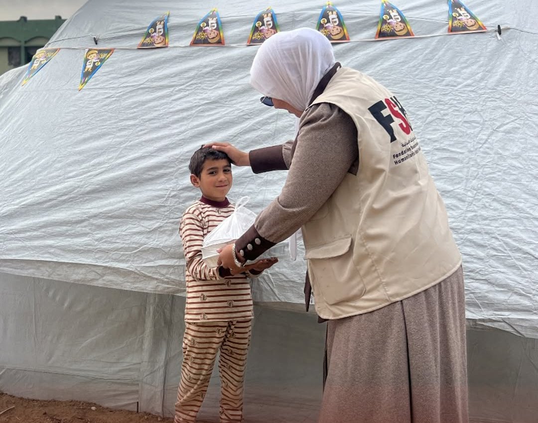An FSH volunteer handing a hot meal to a boy outside a tent in Gaza