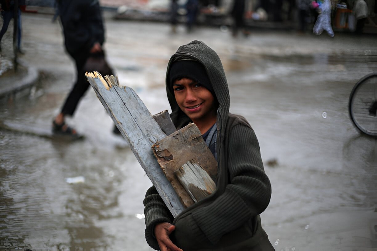 A boy carrying pieces of wood for heating along a flooded street in Gaza